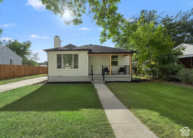 White brick exterior with a dark shingled roof, featuring a covered porch with wood posts and black railings