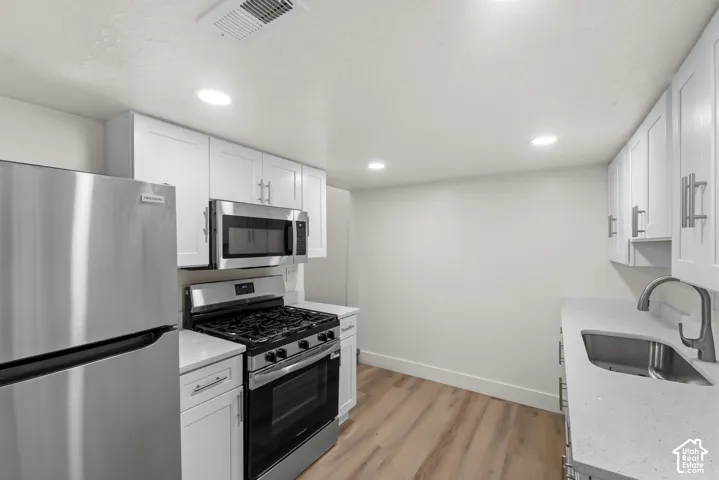 Kitchen featuring white shaker cabinetry, stainless steel appliances, light-toned countertops, wood-finish flooring, and recessed lighting