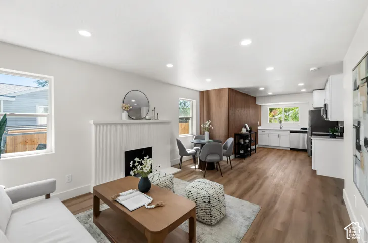 Open-concept living space featuring wood-finish flooring, recessed lighting, a decorative fireplace, and a kitchen with stainless steel appliances and white cabinetry