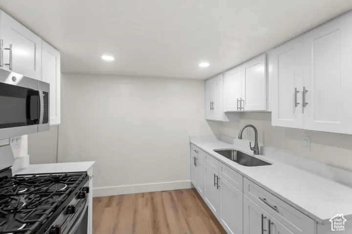 Modern kitchen featuring white shaker cabinetry, stainless steel appliances, light-toned countertops, a stainless steel sink with a gooseneck faucet, and wood-finish flooring