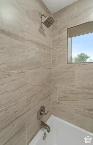 White porcelain tub with a brushed nickel shower head and fixtures, surrounded by large format wall tile