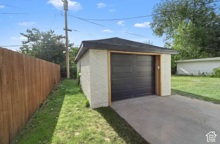 Detached garage featuring a dark panel door, light-toned brick facade, and a shingled roof
