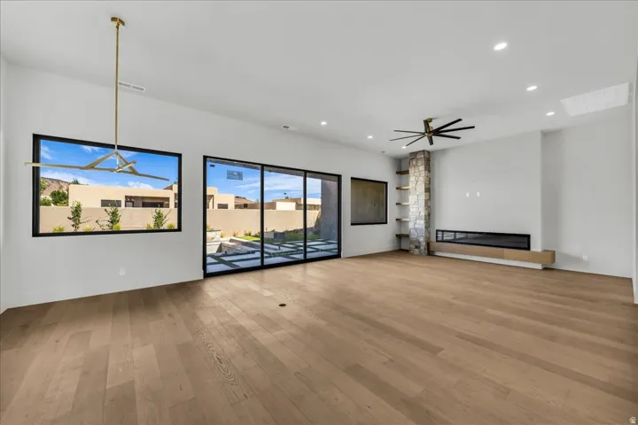Wide-plank wood-finish flooring, linear fireplace with a floating wood mantel, stone-clad pillar with built-in shelving, expansive sliding glass doors, and recessed lighting