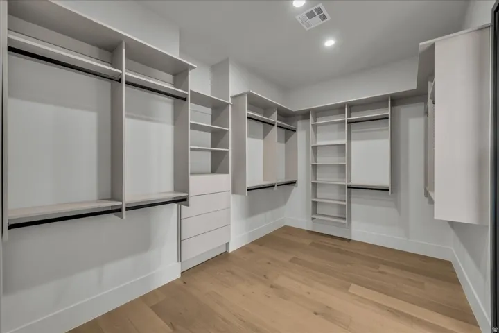 Walk-in closet featuring light wood-finish flooring, recessed lighting, built-in shelving, and multiple hanging rods