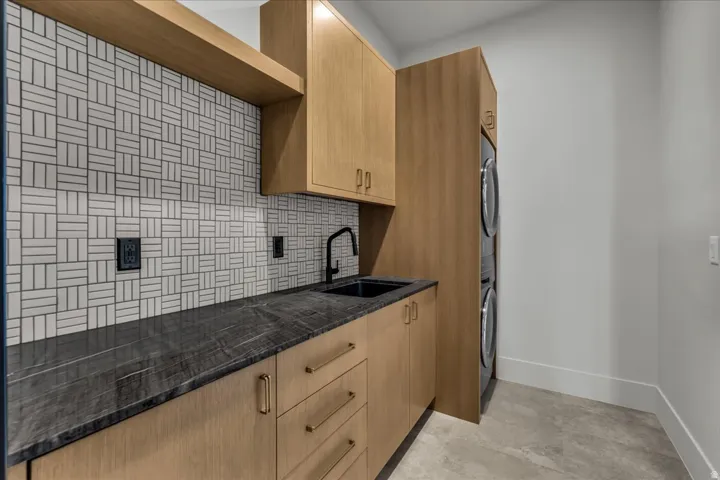 Laundry room featuring a patterned tile backsplash, dark countertop, integrated sink, and wood-finish cabinetry