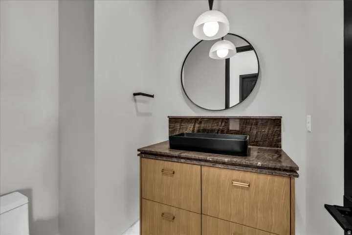 Modern bathroom vanity featuring warm wood-finish cabinetry with multiple drawers, a dark stone countertop, and a sleek rectangular vessel sink