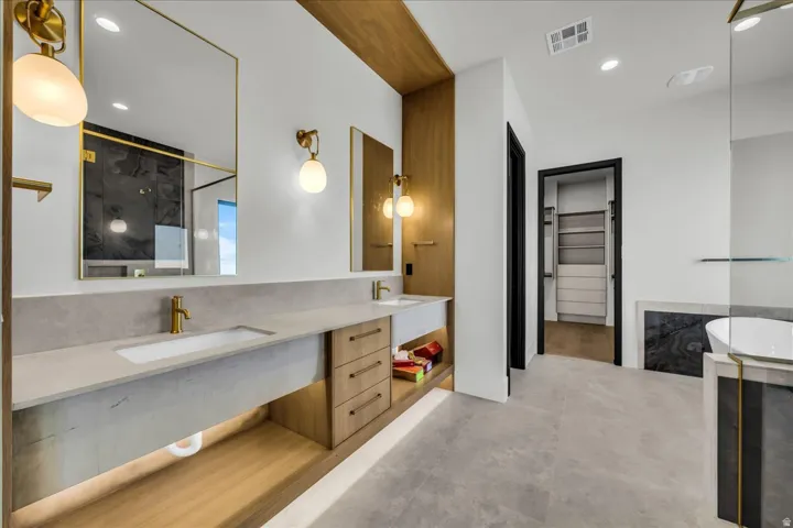Spa-inspired primary bathroom featuring a floating vanity with dual sinks, concrete-finish countertops, and brushed brass hardware