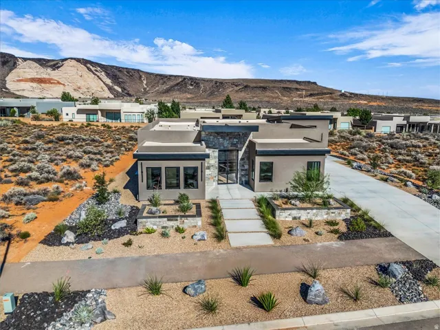 Contemporary desert architecture with a flat roofline, stone veneer accents, an expansive concrete driveway, a paved walkway, and low-maintenance xeriscaping