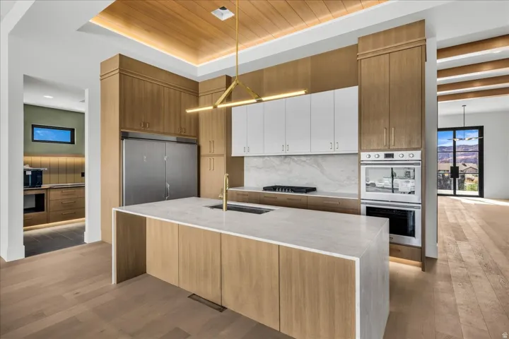 Gourmet kitchen with wood-finish flooring, a waterfall island, integrated stainless steel appliances, and a wood plank ceiling