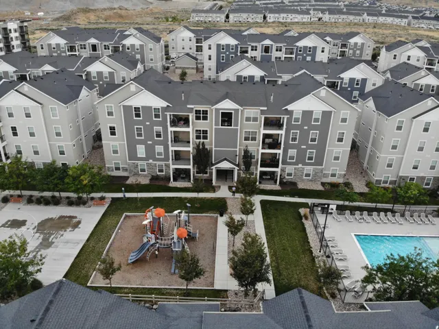 Multi-story apartment building featuring balconies, a communal swimming pool, a playground, and landscaped grounds