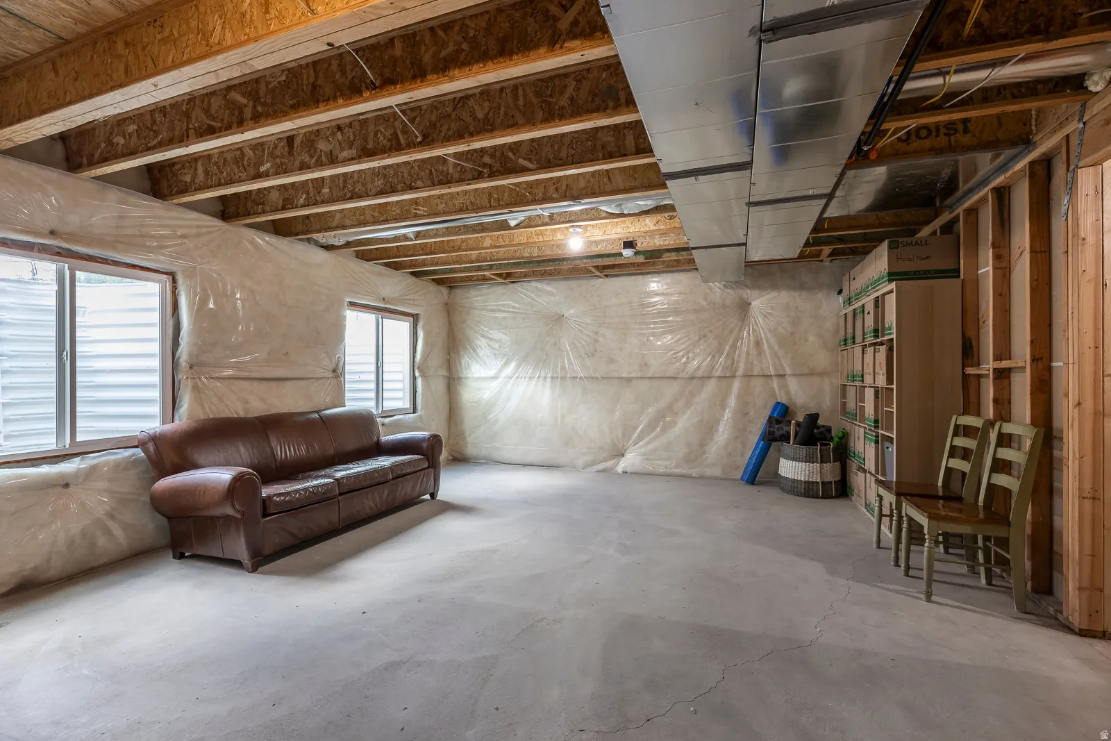Unfinished basement with exposed wood joists, concrete flooring, two windows, and framed walls