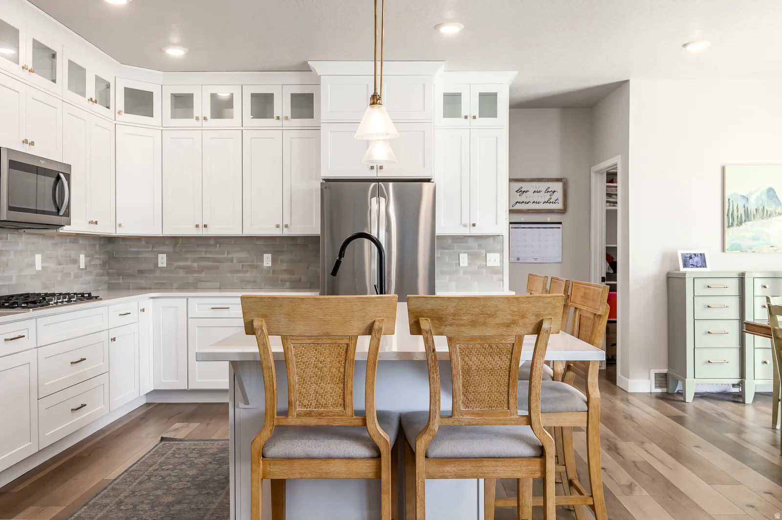 Kitchen featuring white shaker cabinetry, stainless steel appliances, a stone tile backsplash, wood-finish flooring, and a center island with pendant lighting