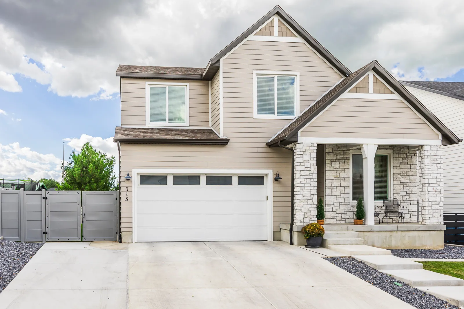 Contemporary exterior featuring siding and stone accents, an attached garage, a covered front porch, and a paved driveway