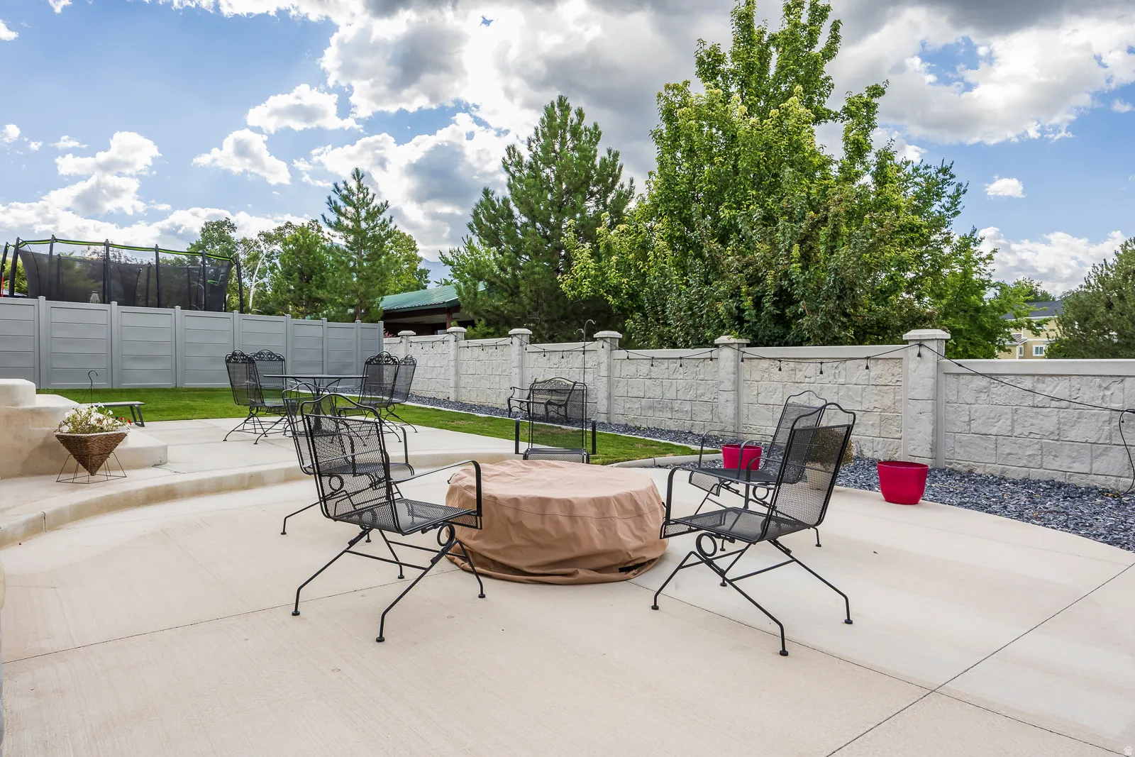 Expansive concrete patio with tiered sections, surrounded by a textured block wall and mature trees