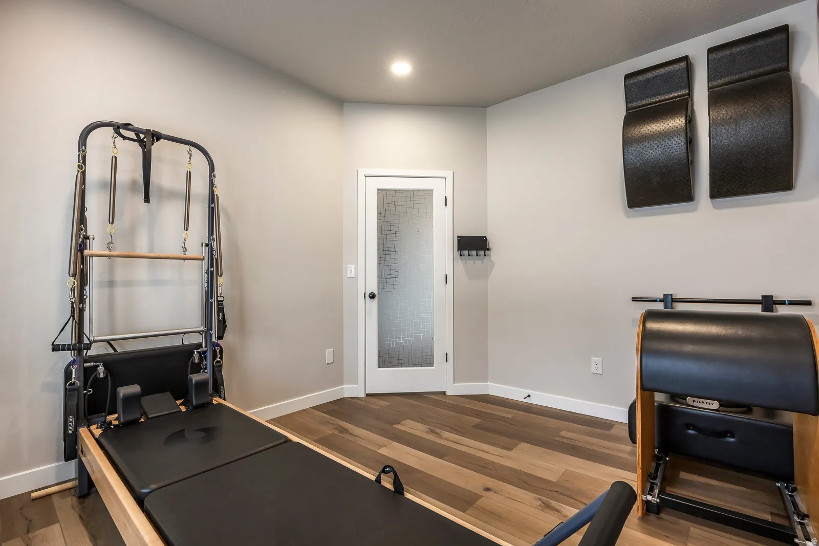 Recessed lighting, wood-finish flooring, white baseboards, and a white interior door with a textured glass panel
