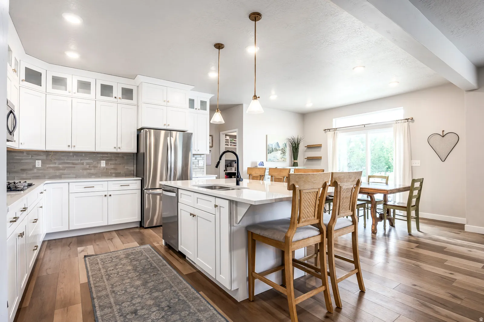 White cabinetry, stainless steel appliances, wood-finish flooring, central island with seating, and a sliding glass door