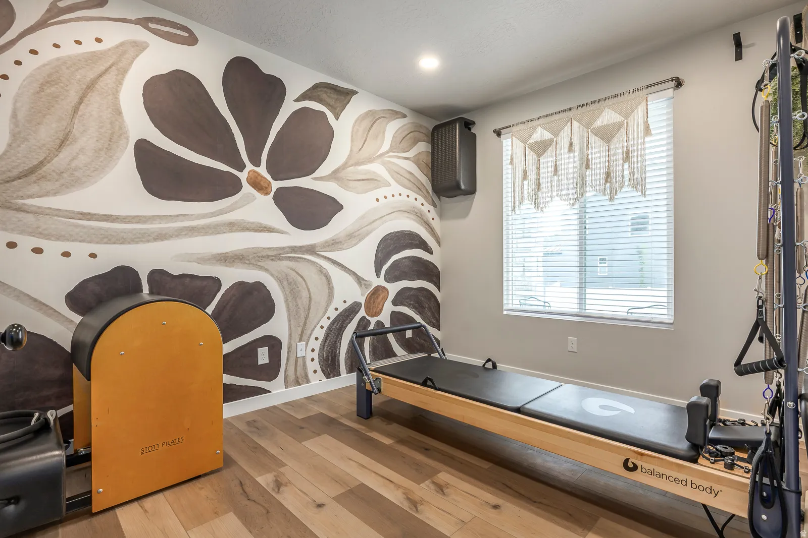 Accent wall with a floral design, wood-finish flooring, recessed ceiling lighting, and a window with blinds