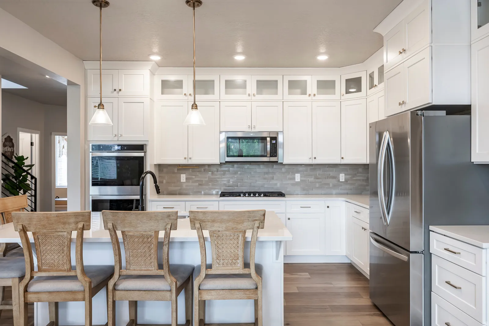 White cabinetry with glass-front upper doors, stainless steel appliances, stone tile backsplash, light-toned wood-finish flooring, and recessed lighting
