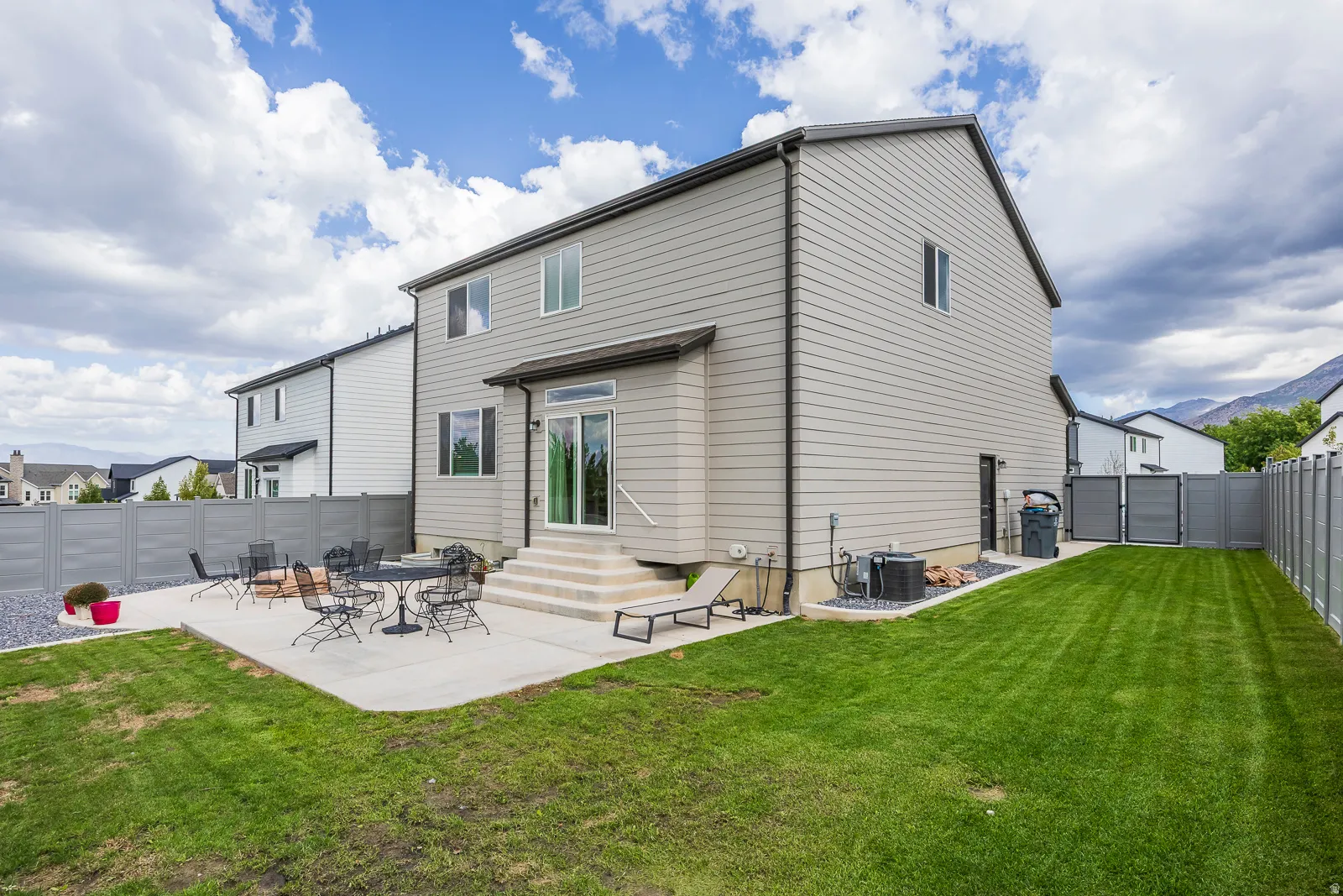 Expansive green lawn with a concrete patio, sliding glass door, privacy fencing, and mountain scenery