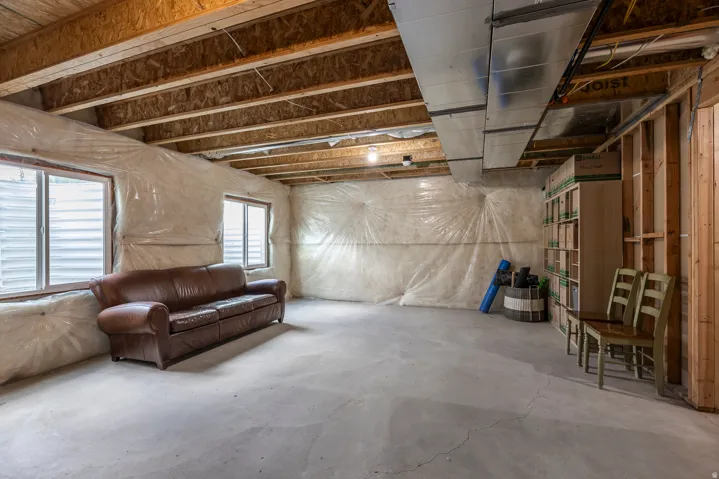 Unfinished basement with exposed wood joists, concrete flooring, two windows, and framed walls