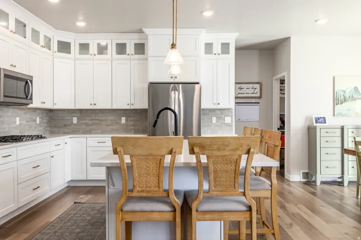 Kitchen featuring white shaker cabinetry, stainless steel appliances, a stone tile backsplash, wood-finish flooring, and a center island with pendant lighting