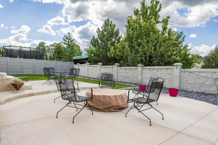 Expansive concrete patio with tiered sections, surrounded by a textured block wall and mature trees