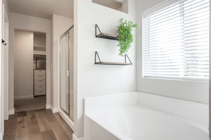 Deep soaking tub with a white tile surround, wood-finish flooring, and a glass-enclosed shower
