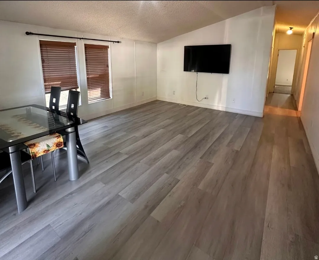 Wood-finish flooring throughout, paired with white walls, and dual windows featuring brown blinds