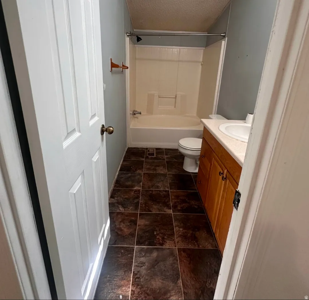 White paneled door, wood-finish vanity, integrated sink, shower-tub combination, and dark tile flooring