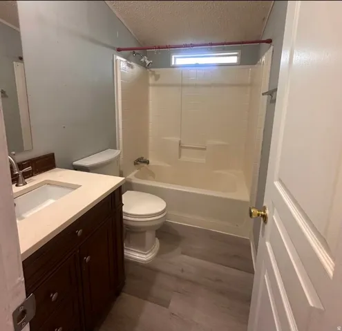 Vanity with integrated rectangular sink and brass-finish faucet, white toilet, and tub-shower combination with an opaque window