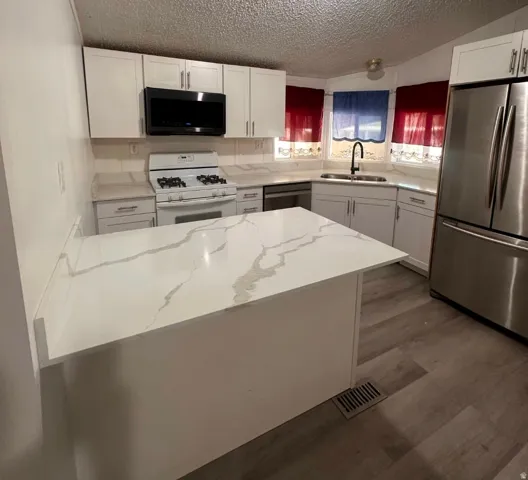 White cabinetry, quartz countertops with integrated backsplash, stainless steel refrigerator, white gas range with overhead microwave, and wood-finish flooring