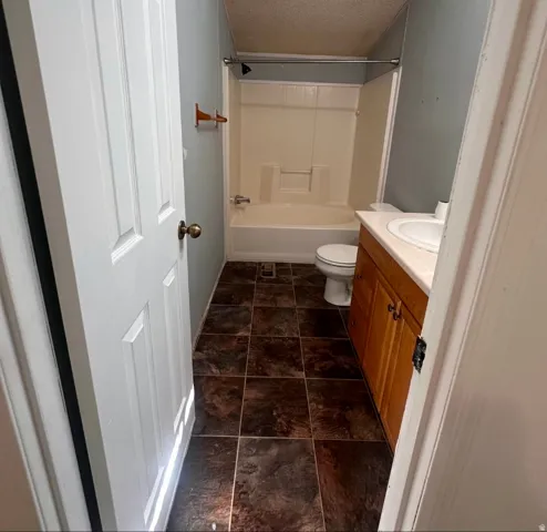 White paneled door, wood-finish vanity, integrated sink, shower-tub combination, and dark tile flooring