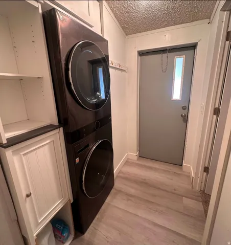 Integrated stackable washer and dryer, wood-finish flooring, white built-in cabinetry with dark countertop, and a gray door with an integrated window
