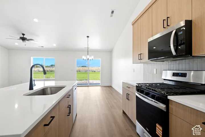 Kitchen featuring wood-finish cabinetry, stainless steel appliances, a white solid surface countertop island with an undermount sink and matte black faucet, and wood-finish flooring