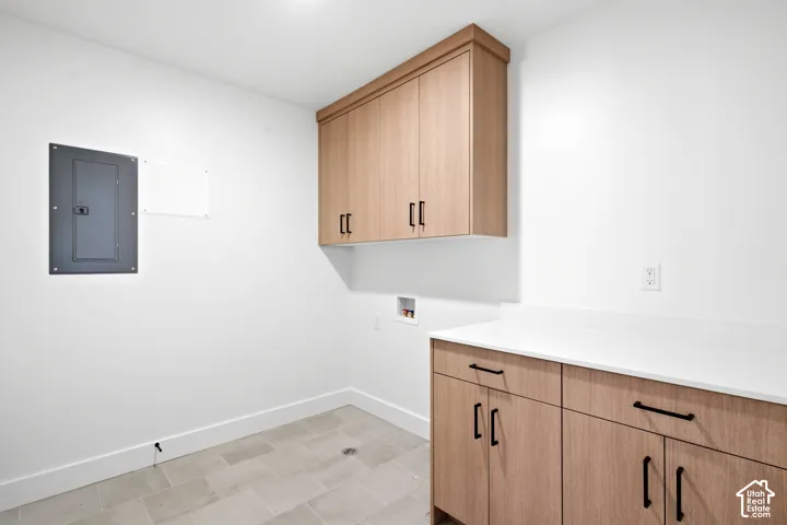 Light-toned wood-finish cabinetry with black hardware, white countertops, tile flooring, and a ceiling-mounted light fixture