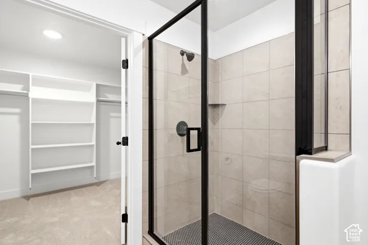 Walk-in closet with built-in shelving, glass-enclosed shower, tiled shower walls, black-framed shower door, and black shower fixtures