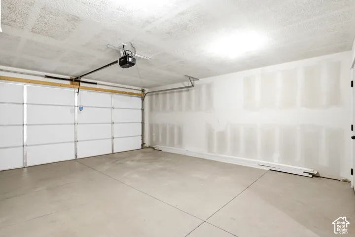 Concrete flooring, white paneled garage door, exposed ceiling joists, overhead lighting, finished interior walls