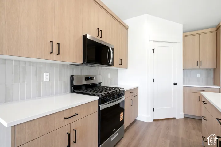 Modern kitchen featuring light wood-finish cabinetry, stainless steel appliances, white countertops, and a full-height tile backsplash