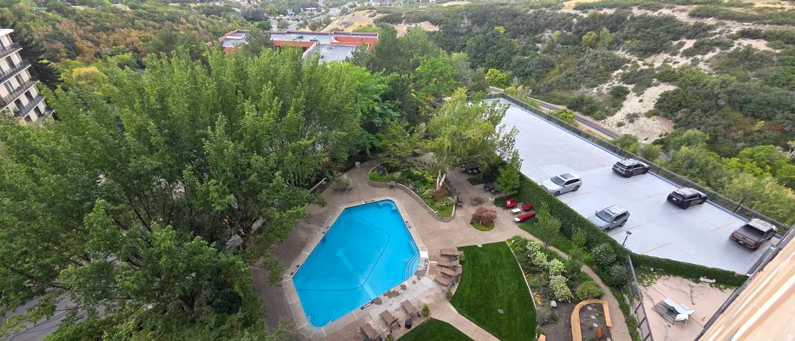 Outdoor swimming pool with surrounding hardscaping, mature trees, and landscaped green spaces