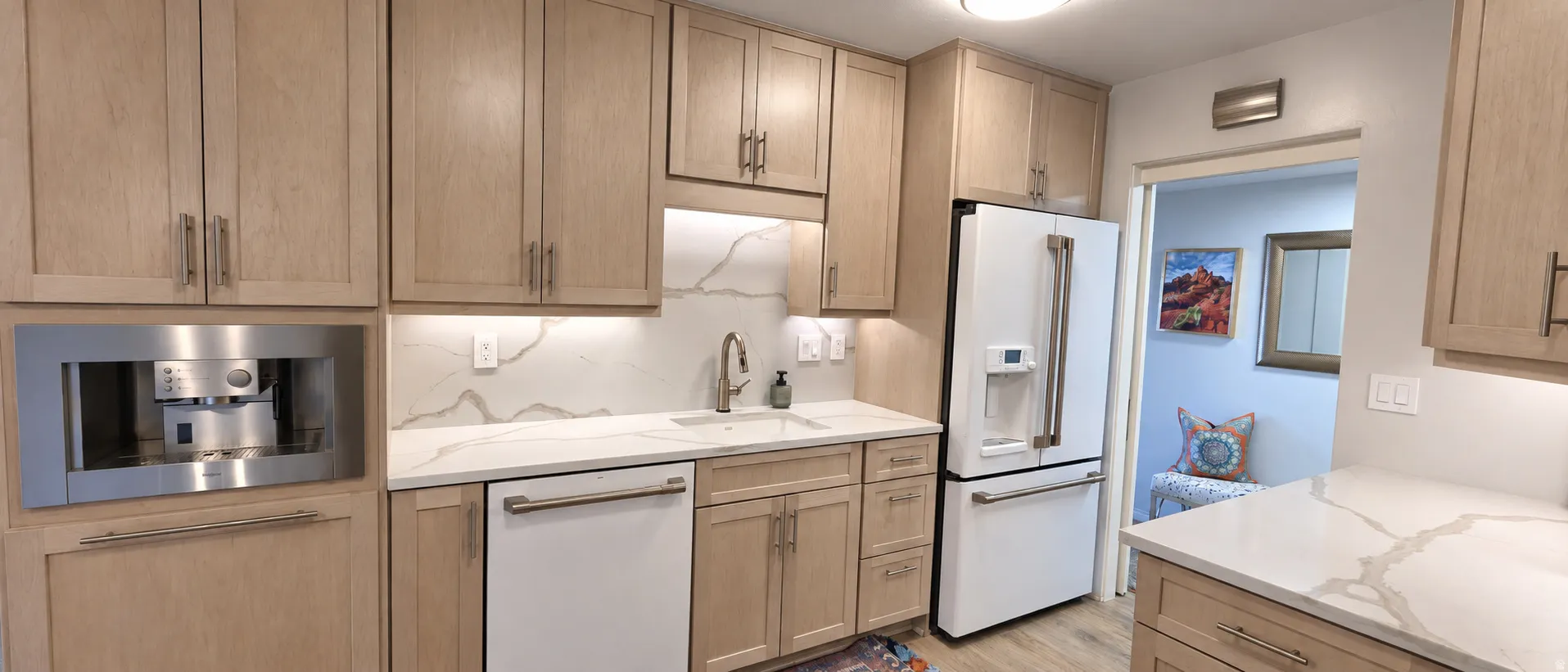 Kitchen featuring light wood-finish cabinetry, white countertops with veining, a built-in espresso machine, a large white refrigerator, and an undermount sink