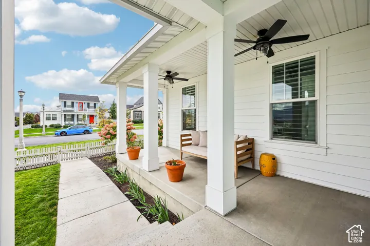 Covered front porch with recessed lighting and two ceiling fans, featuring a concrete walkway, white picket fence, and manicured lawn