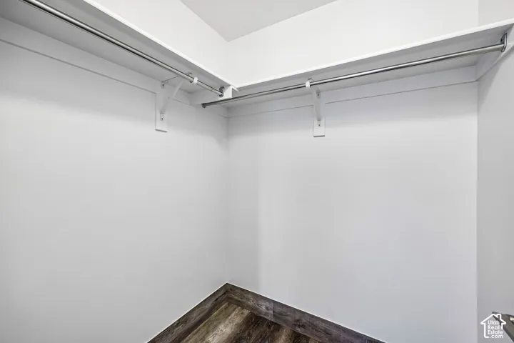 Walk-in closet featuring white shelving, chrome hanging rods, laminate flooring
