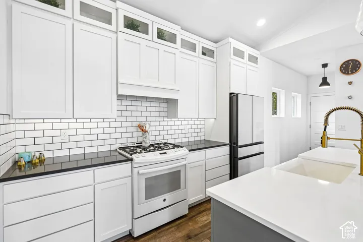 White shaker-style cabinetry with upper glass-front cabinets, subway tile backsplash, dark countertops, white gas range.
