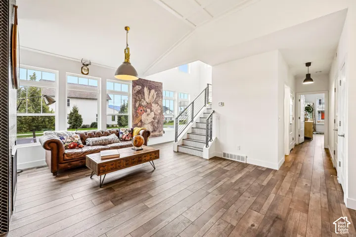 Vaulted ceiling with decorative ceiling detail, laminate flooring, multiple large windows, custom tiled riser staircase with metal railing, and a hallway featuring custom pendant lighting