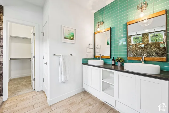 Dual vessel sinks with individual mirrors, custom teal tile backsplash, white shaker-style cabinetry, dark countertop, and laminate flooring