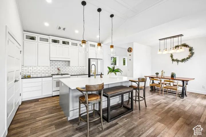Open-concept kitchen and dining area featuring laminate flooring, white cabinetry with upper glass-front display cabinets, white subway tile backsplash, quartz countertops.