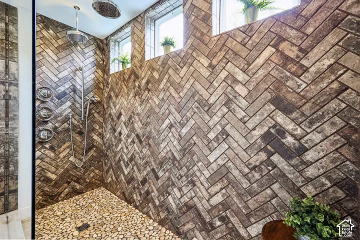 Primary bathroom with custom herringbone-patterned tile walls, pebble floor, wall-mounted shower controls, and dual shower heads
