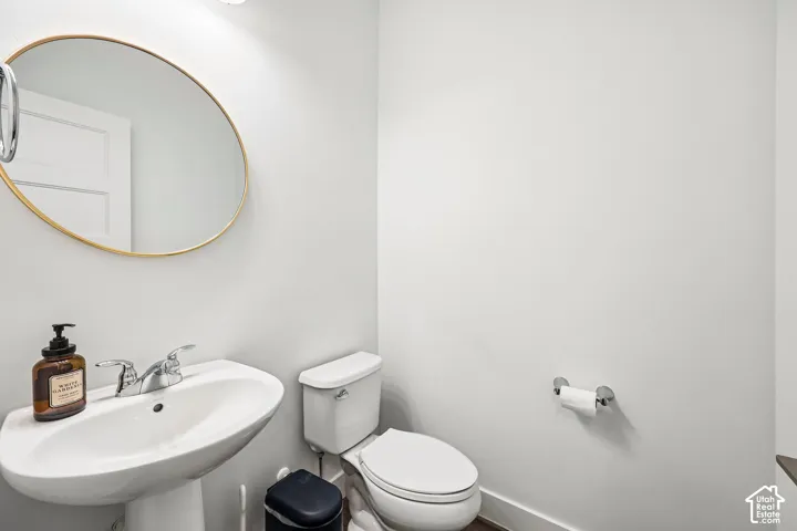 Pedestal sink with chrome faucet, round gold-framed mirror, and white walls