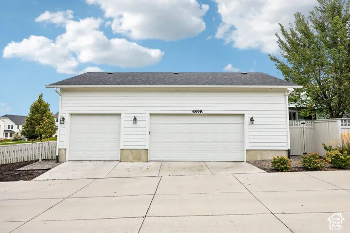 3 car garage with white paneled doors, white siding, and exterior wall sconces