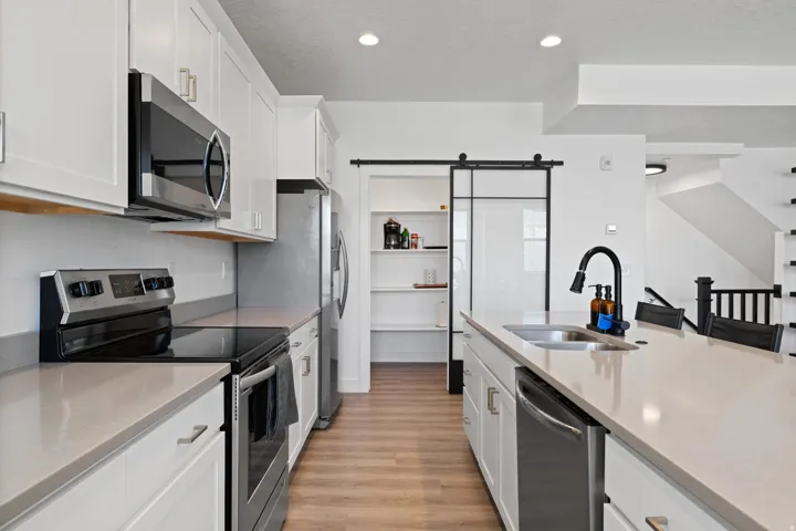 Contemporary kitchen featuring white cabinetry, stainless steel appliances, a center island with sink, wood-finish flooring, and a pantry with a sliding barn door
